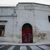 La struttura presenta al centro un arco in pietra che racchiude il rosso portone di ingresso serrato da un lucchetto...
